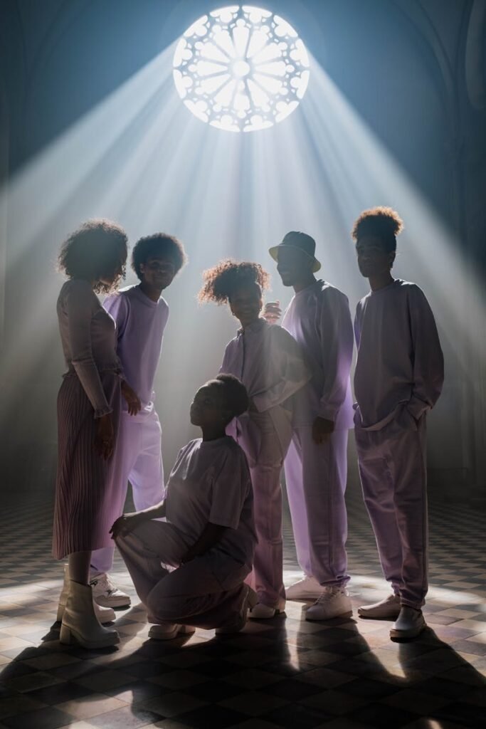 A group of adults in lavender outfits stand dramatically backlit by rays from a church window.