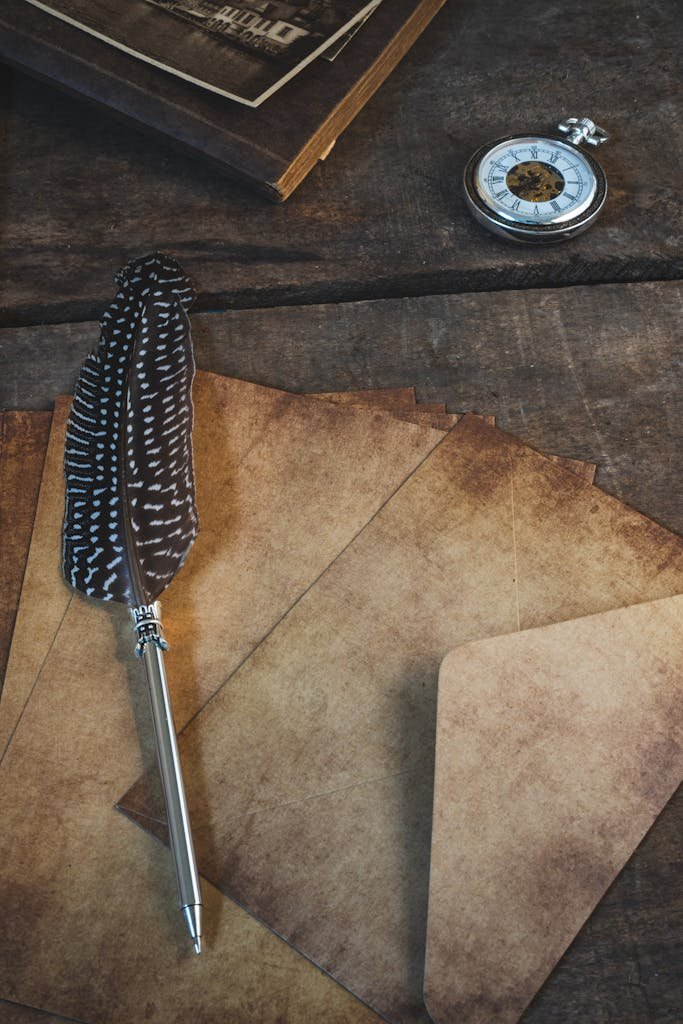 Quill pen with envelopes and pocket watch on rustic wooden table, exuding vintage charm.